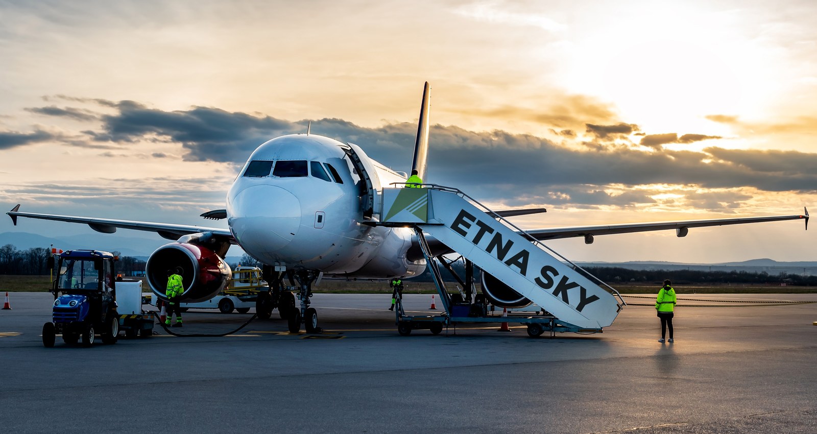 etna-sky-aereo-anteprima Rendering di un aeromobile con livrea Etna Sky” - Aereo sul piazzale aeroportuale al tramonto con scala d’imbarco personalizzata Etna Sky_generata con AI